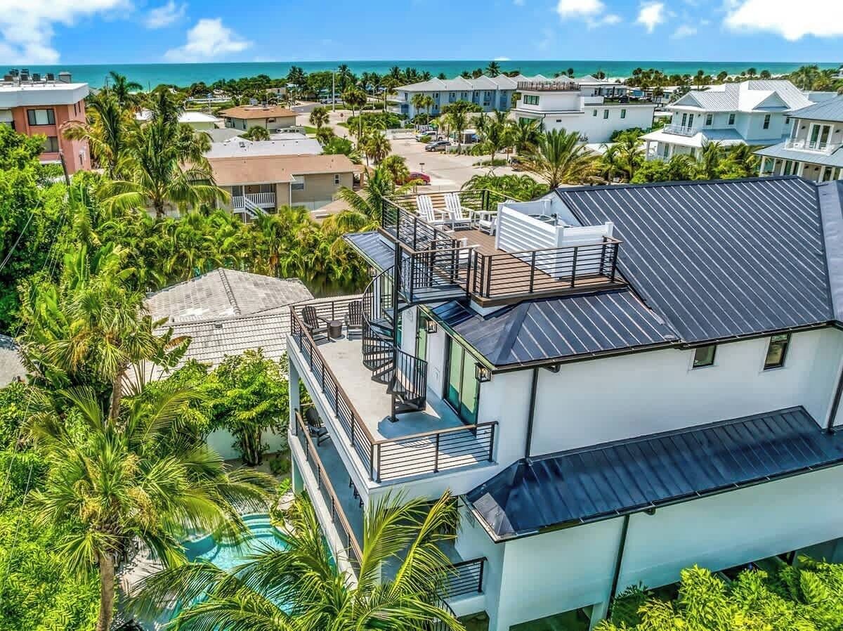 A multi-story building with a rooftop deck, surrounded by palm trees and a view of the ocean.