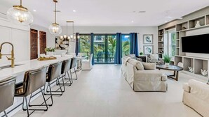 A modern living room with a sofa, a coffee table, and a TV. There is a kitchen area with a bar and chairs. - Walk to St. Armands and Lido Key Beach/Gulf Views (Sarasota)