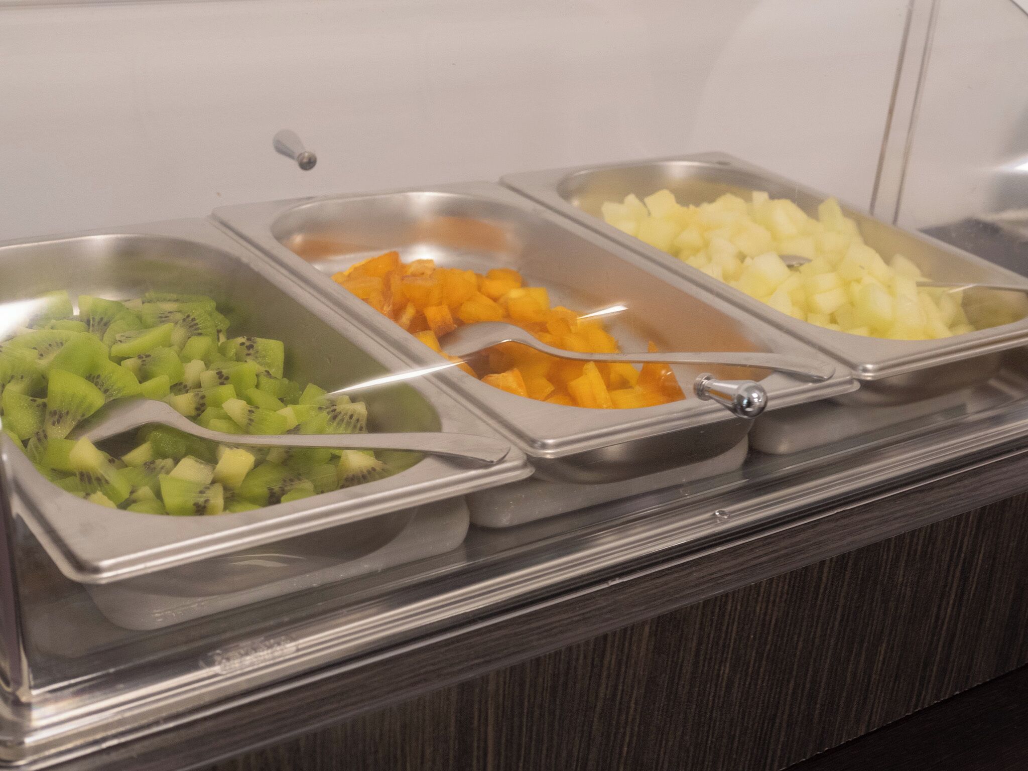 A buffet with three metal trays containing sliced fruits.