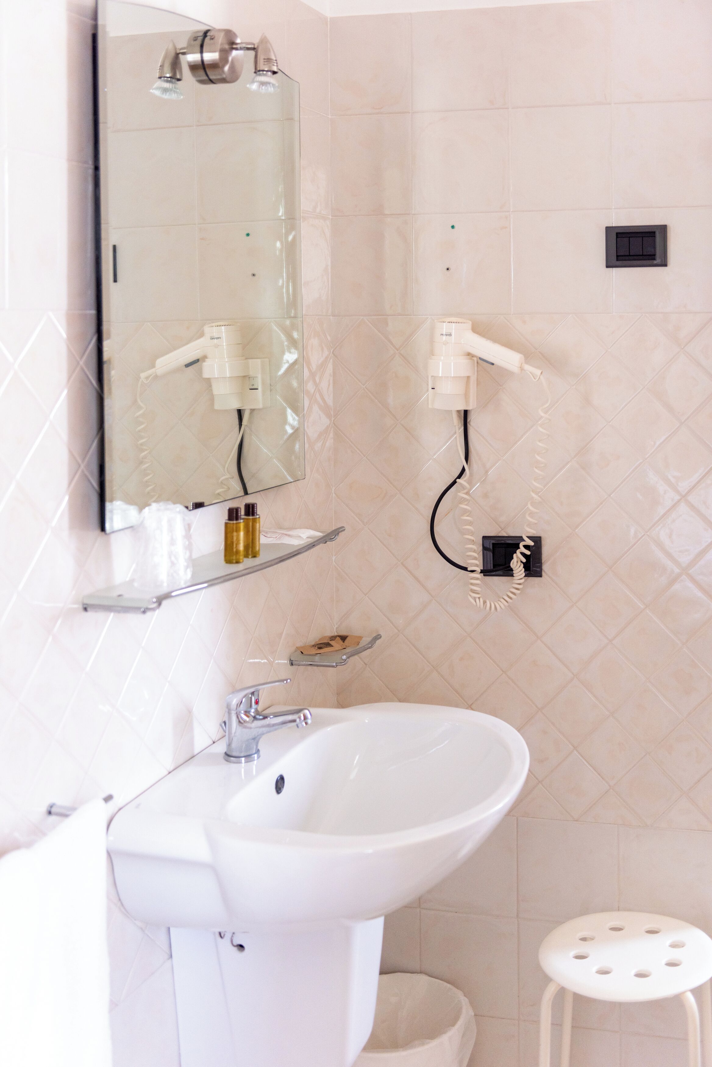 A bathroom with a white sink, a mirror, a hairdryer, and a small stool.