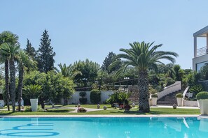 A swimming pool surrounded by palm trees and a stone wall. - Villa Maria (Crispiano)