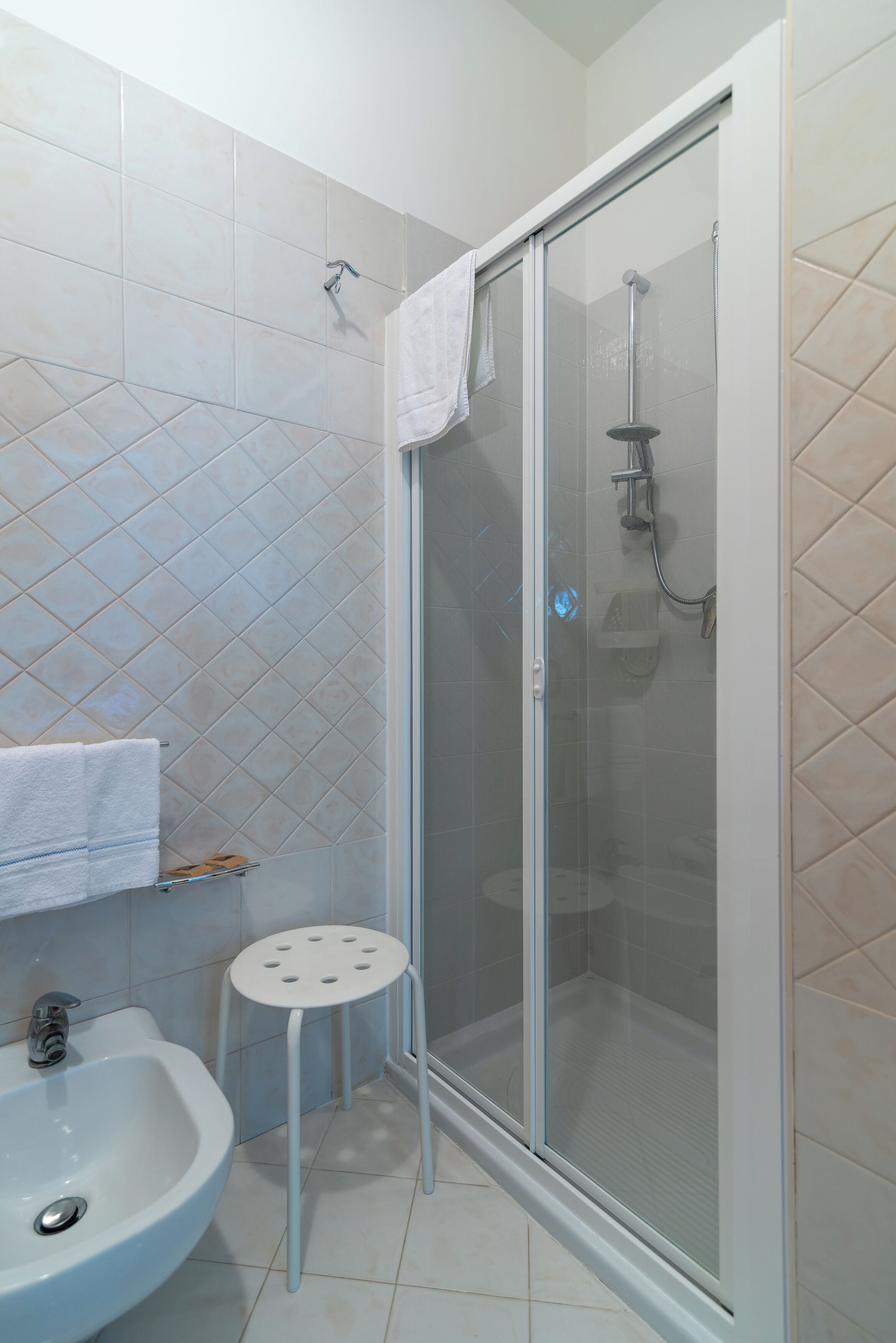 Un baño con ducha de vidrio, un lavabo y un taburete pequeño.