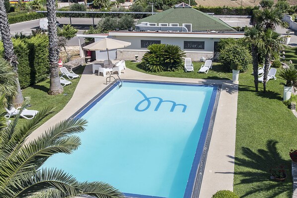 Une piscine ornée d’un logo, entourée de palmiers et de chaises longues.