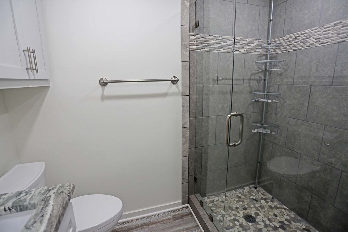 A bathroom with a white toilet, a glass shower enclosure, and a tiled floor.