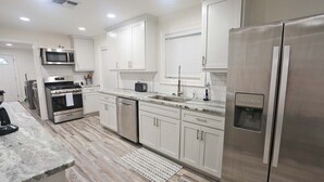 A modern kitchen with stainless steel appliances, white cabinetry, and a marble countertop. - Flying Fish Yellow Fin-Beach Access-Island Realty (Grand Isle)
