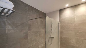 Un baño moderno con cabina de ducha de vidrio, baldosas de piedra oscura y un perchero para toallas.