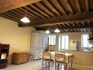 A rustic kitchen with wooden beams, a stove, a dining table with chairs, and a white cabinet.