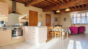 Une cuisine dotée d’un îlot central, de poutres apparentes en bois au plafond et d’un coin repas avec une table et des chaises.
