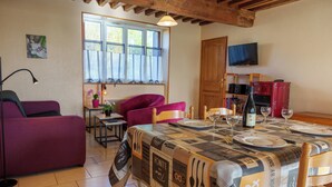 Un coin repas avec une table dressée pour quatre personnes, un canapé violet et un téléviseur fixé au mur.