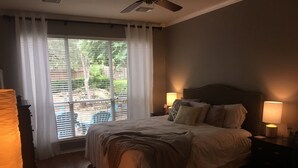 Un dormitorio con cama, dos lámparas de noche, ventilador de techo y ventana con persianas.