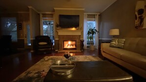 Una sala de estar con chimenea, un sofá, una mesa de centro y un televisor montado en la pared.