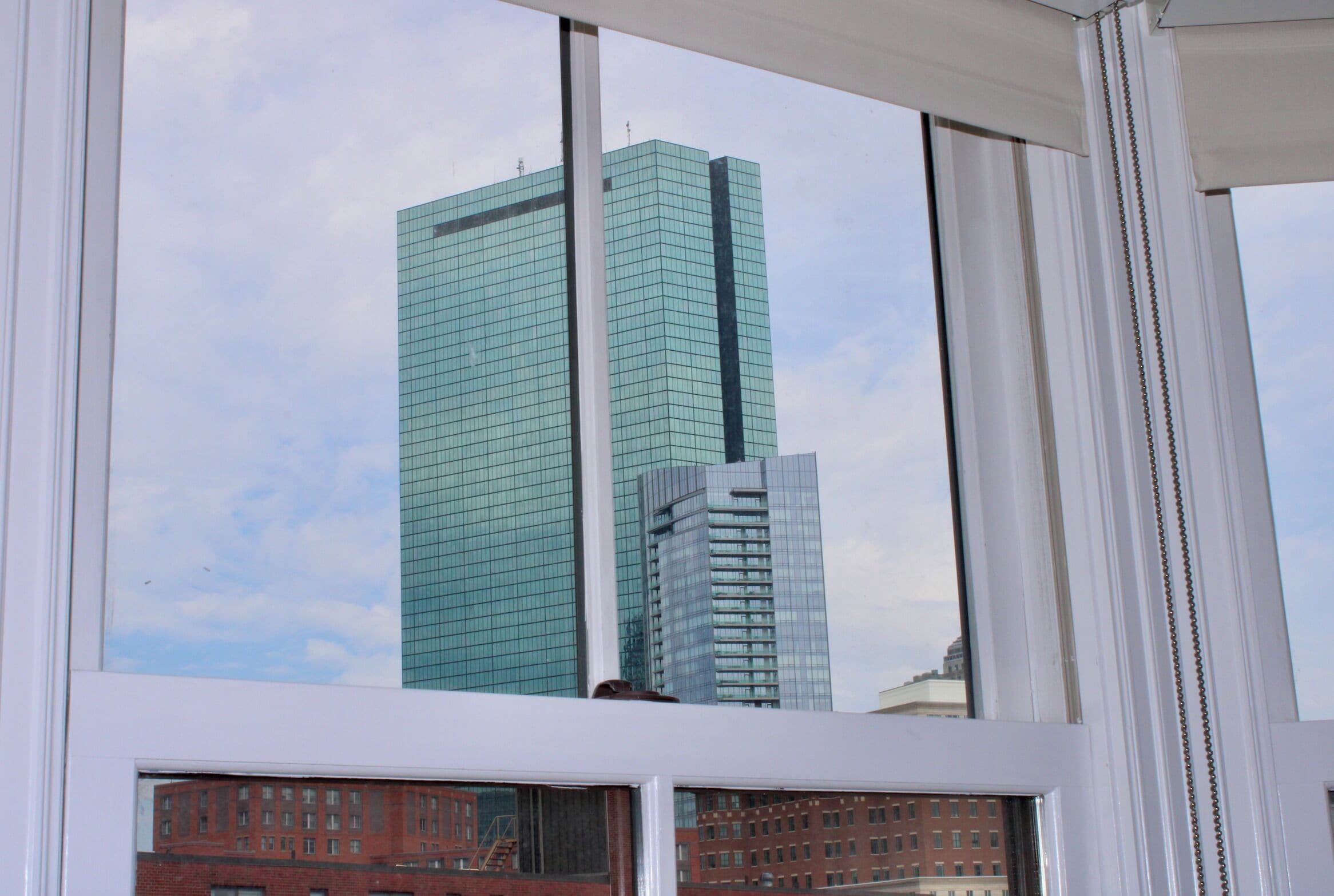 Vista a través de una ventana de un edificio alto de vidrio, con el reflejo de un edificio de ladrillo rojo abajo.