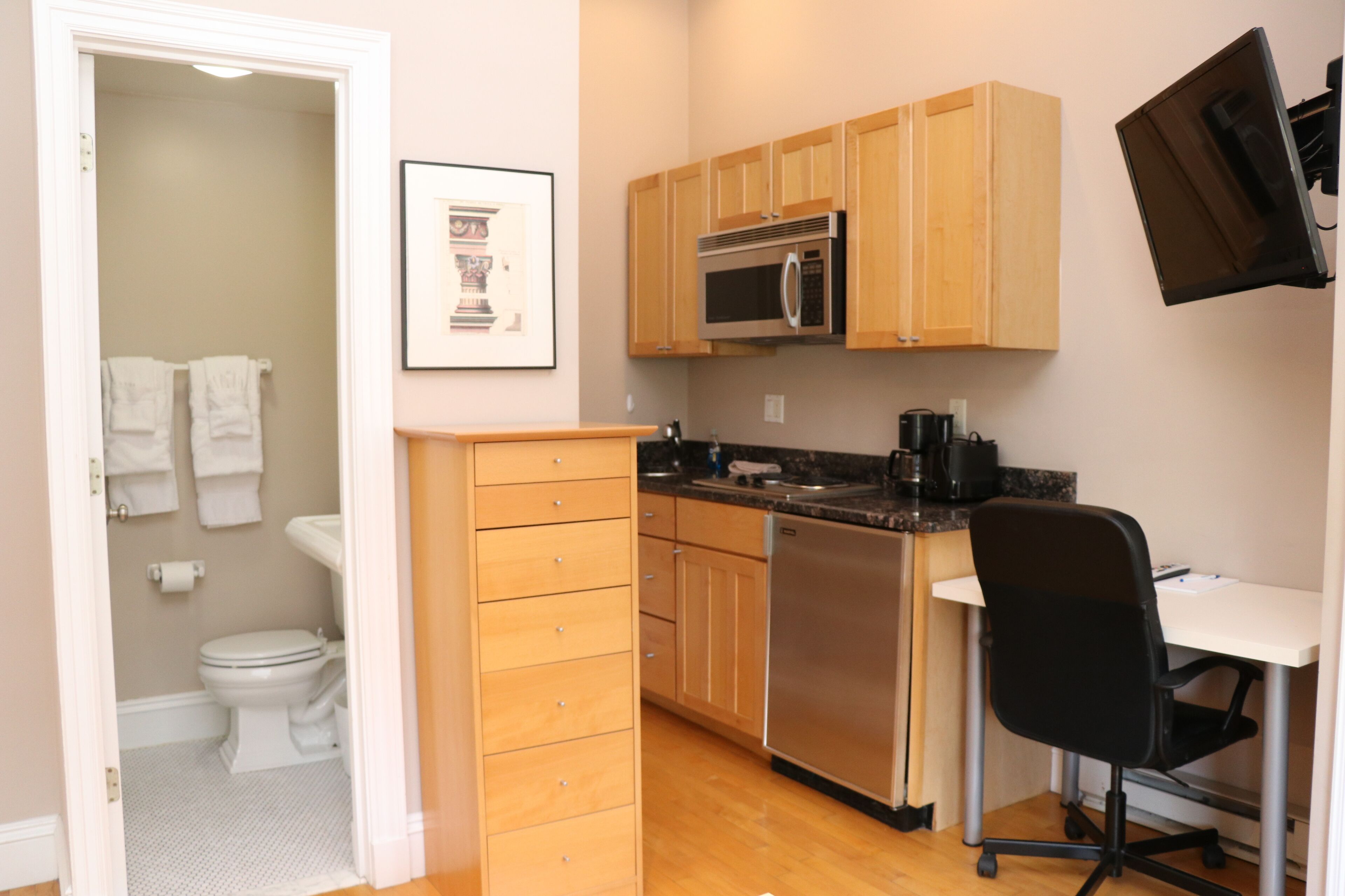 A compact kitchen with wooden cabinets, a microwave, a dishwasher, and a small office area with a chair.