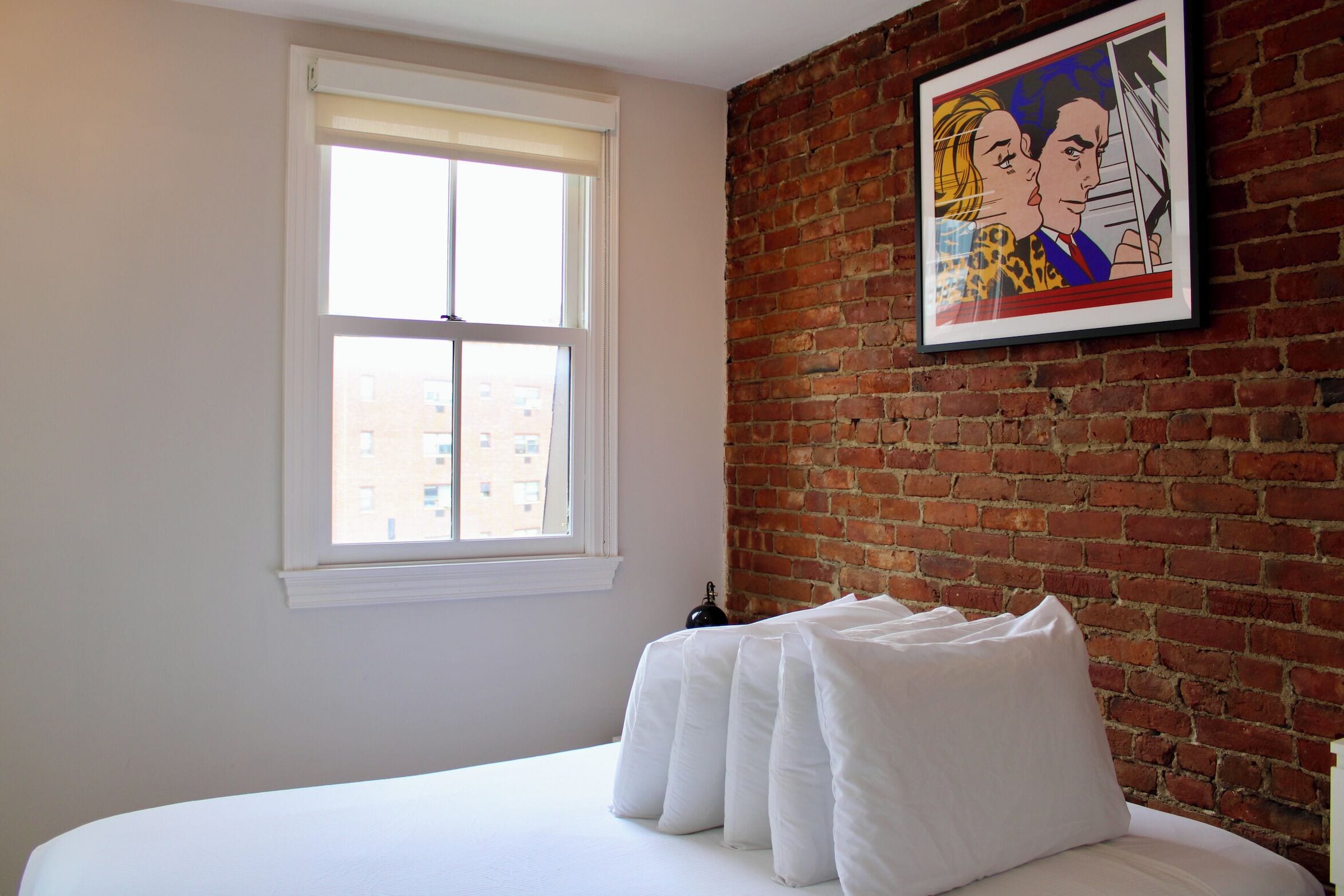 A hotel room with a brick wall, a window, and a bed with white bedding.