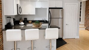 A modern kitchen with white cabinets, a stainless steel refrigerator, and three white bar stools. - Maverick Suites at 402 Columbus Ave (Boston)