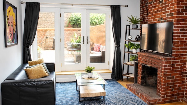 A living room with a black leather sofa, a glass coffee table, a brick fireplace, and a TV mounted on the wall. - Maverick Suites at 402 Columbus Ave (Boston)