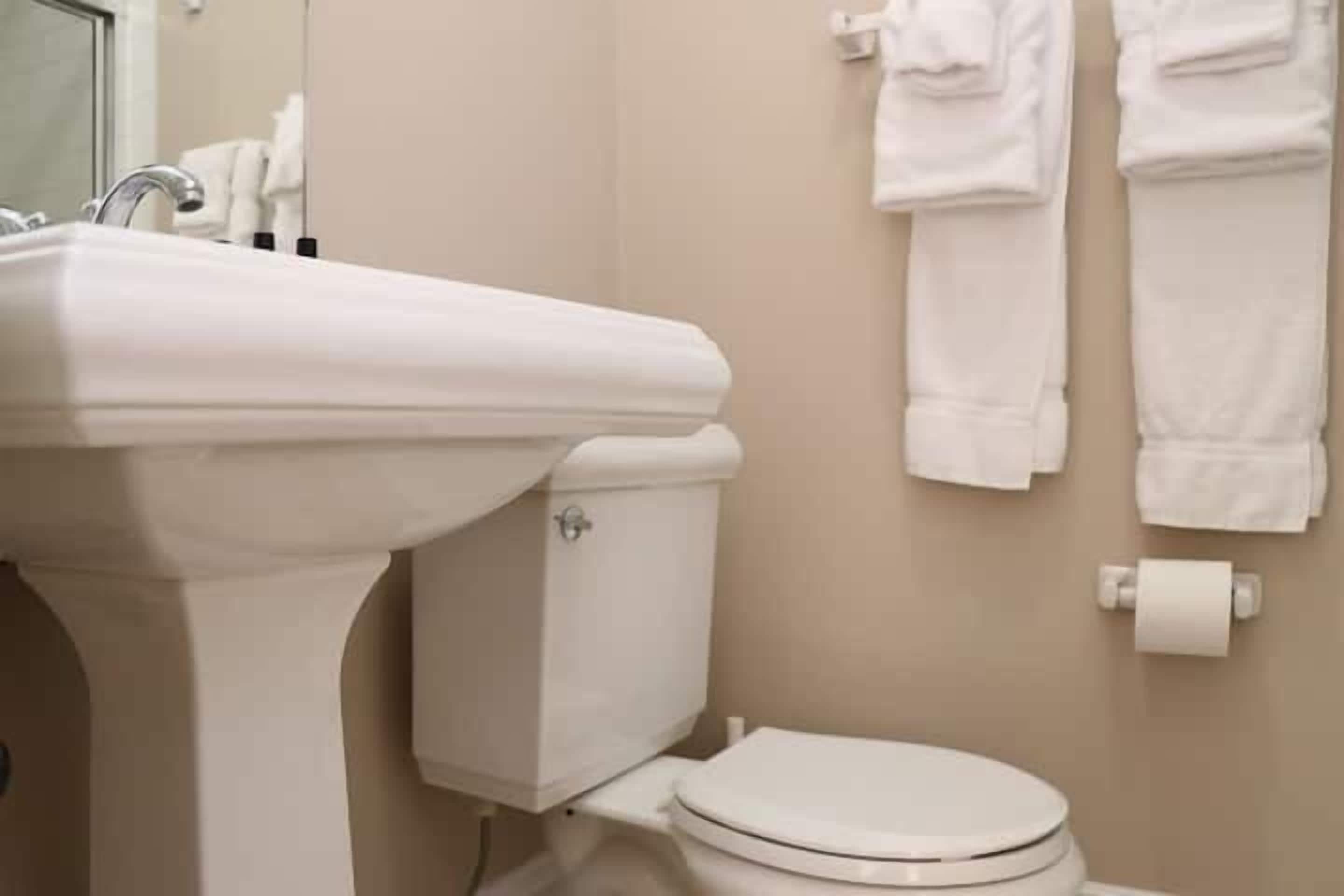 A bathroom with a white sink, toilet, and towels hanging on the wall.