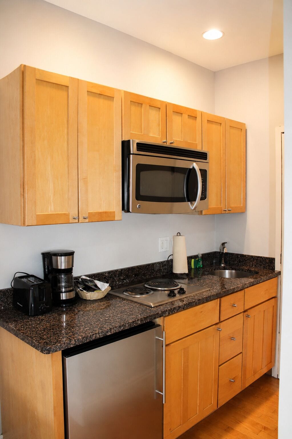 A kitchen with wooden cabinets, a stainless steel microwave, a coffee maker, a toaster, and a sink.