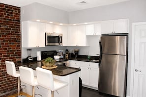 A modern kitchen with white cabinets, stainless steel appliances, and a brick accent wall. - Maverick Suites at 402 Columbus Ave (Boston)