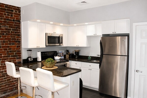 A modern kitchen with white cabinets, stainless steel appliances, and a brick accent wall.