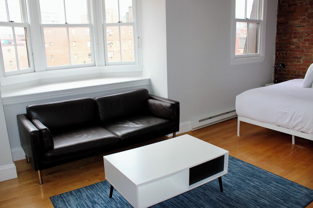 A modern bedroom with a black leather sofa, a white bed, and a white TV stand.