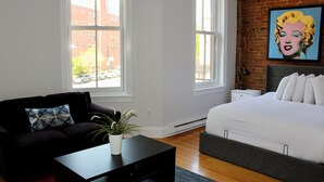 A bedroom with a bed, a couch, a small table, and a window. - Maverick Suites at 402 Columbus Ave (Boston)