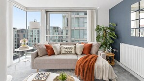 A modern living room with a sofa, a coffee table, and a view of the cityscape through large windows.
