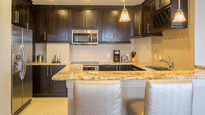 A modern kitchen with dark wood cabinets, a stainless steel refrigerator, a microwave, a double sink, and a granite countertop. - Adventure Park Vacation 1 BR Condo with Tropical Pool (Orlando)