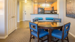 A dining area with a round table and four chairs, a kitchen in the background, and a door leading to another room. - Adventure Park Vacation 1 BR Condo with Tropical Pool (Orlando)