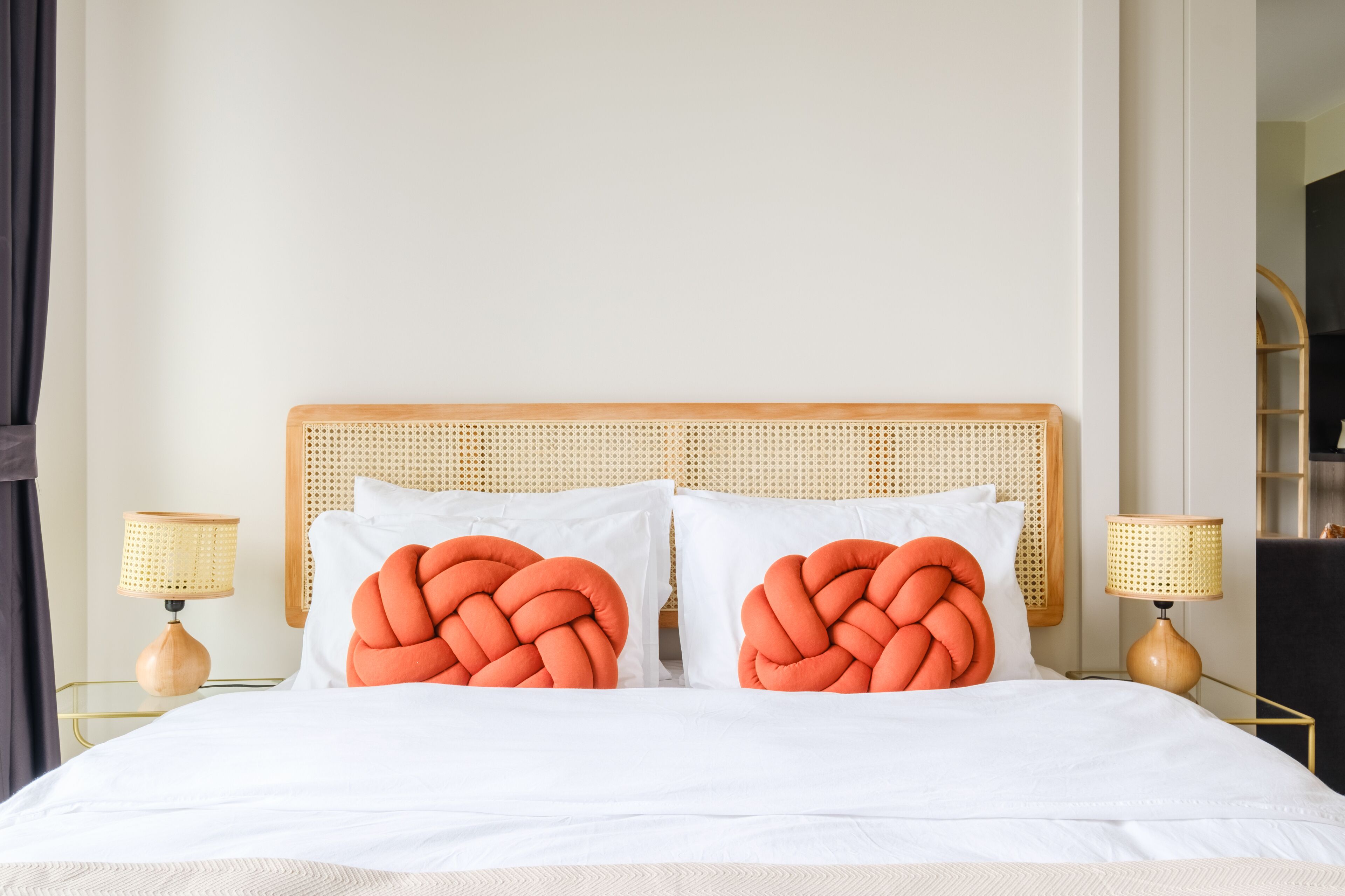 Una cama con ropa de cama blanca y dos almohadas naranjas, flanqueada por dos mesitas de noche con lámparas.
