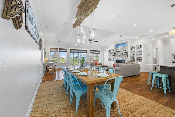 Une salle à manger spacieuse avec une table en bois et des chaises bleues, une cuisine avec des meubles blancs et un salon doté d’un canapé gris.
