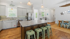 A modern kitchen with white cabinets, a large island with bar stools, wooden flooring, and pendant lighting. - Bonny Blue:  Gorgeous SGI Home, Pet Friendly, Private Pool,  Sleeps 14 (St. George Island)