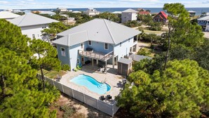 A two-story house with a swimming pool, surrounded by trees and a view of the ocean. - Bonny Blue:  Gorgeous SGI Home, Pet Friendly, Private Pool,  Sleeps 14 (St. George Island)