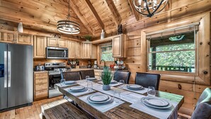 A wooden cabin interior with a dining table set for six, a refrigerator, microwave, and stove.