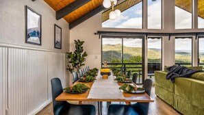 A dining area with a wooden table set for six, surrounded by black chairs, with a view of a mountainous landscape through large windows. - 🌙 Crescent Chalet - Hot Tub, Views, Sauna! (Oakhurst)