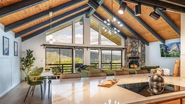 A spacious kitchen with a large island, wooden beams, and a stone fireplace. - 🌙 Crescent Chalet - Hot Tub, Views, Sauna! (Oakhurst)