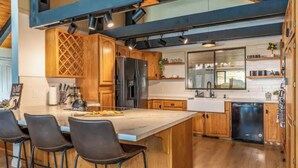 A modern kitchen with wooden cabinets, a large island with bar stools, and a dishwasher. - 🌙 Crescent Chalet - Hot Tub, Views, Sauna! (Oakhurst)