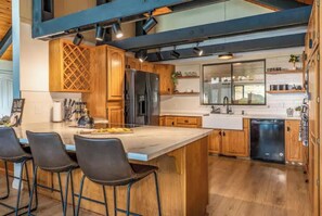 Cocina moderna con armarios de madera, una isla grande con taburetes de bar y lavavajillas.
