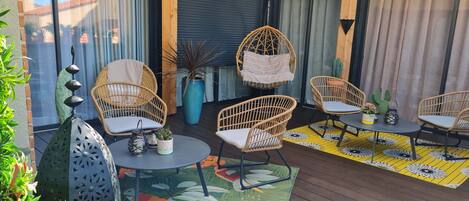 A wooden deck with wicker furniture, a round table, and a potted plant.