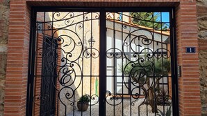 A wrought iron gate with intricate designs, a brick wall, and a clear blue sky. - Charming town center residence with terrace and view of the Canigou mountains (Thuir)