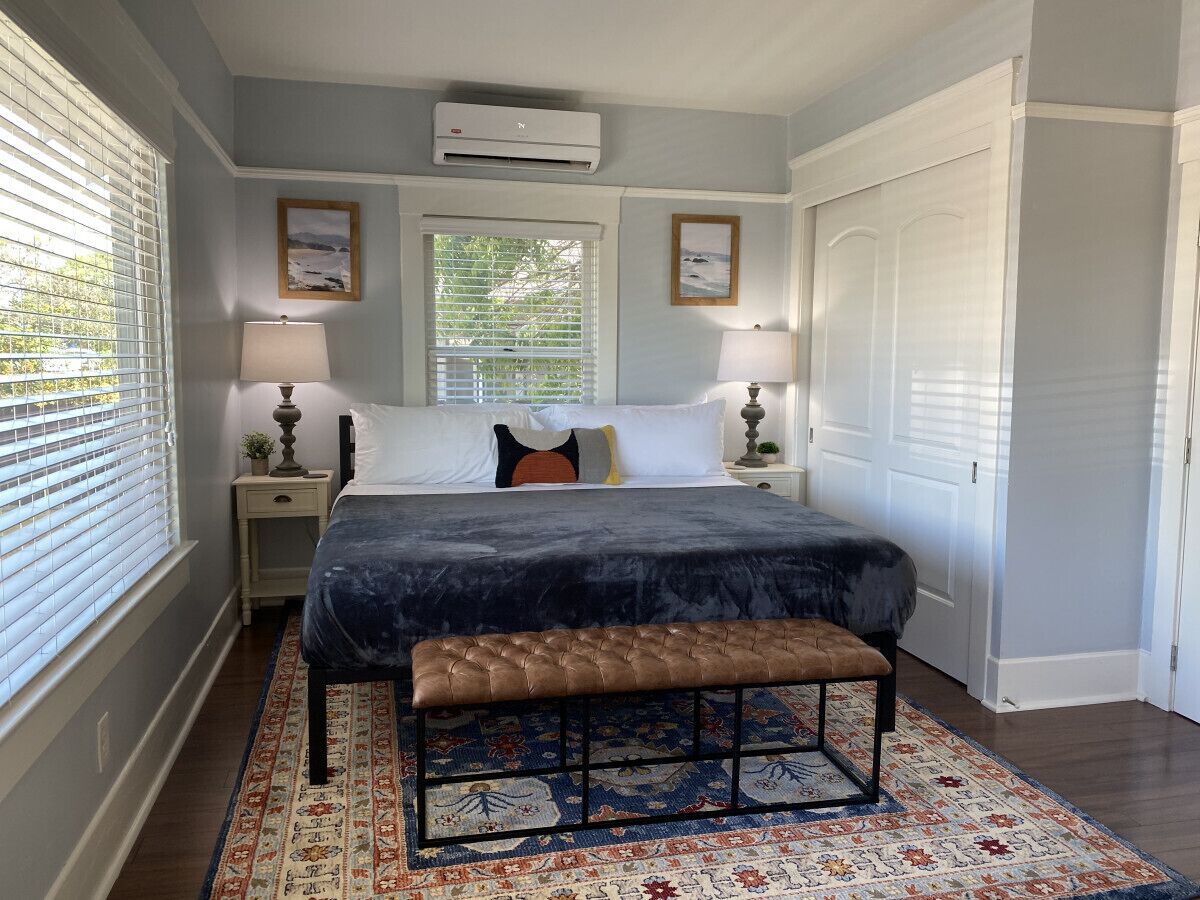 Une chambre à coucher comprenant un lit, deux tables de chevet, un banc, un tapis à motifs et une porte.