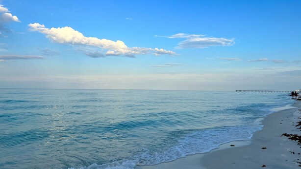 A beach with clear blue water, a sandy shore, and a pier in the distance. - Life is Better at the BEACH! Beautifully decorated and freshly updated retreat! (Panama City Beach)
