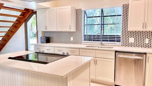 A modern kitchen with white cabinetry, a built-in stove, a dishwasher, and a window with blinds. - Treasure Coast Retreat (Fort Pierce)