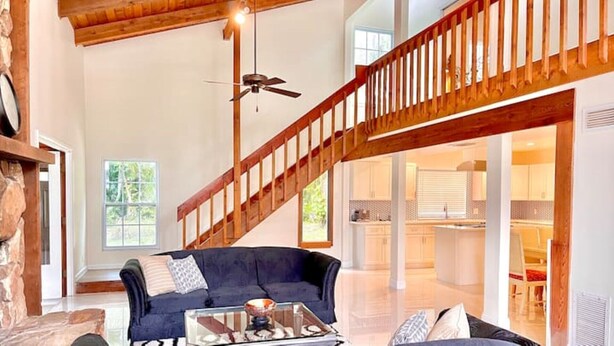 A spacious living area with a dark blue sofa, a glass coffee table, and a wooden staircase leading to an upper level. - Treasure Coast Retreat (Fort Pierce)