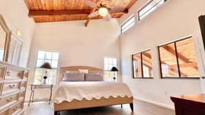 A spacious bedroom with a large bed, wooden ceiling beams, and multiple windows. - Treasure Coast Retreat (Fort Pierce)