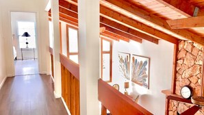 A hallway with wooden beams, a staircase, and a stone wall with artwork. - Treasure Coast Retreat (Fort Pierce)