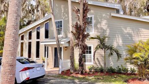 A two-story building with a front porch, a white car parked in front, and a palm tree in the yard. - Treasure Coast Retreat (Fort Pierce)