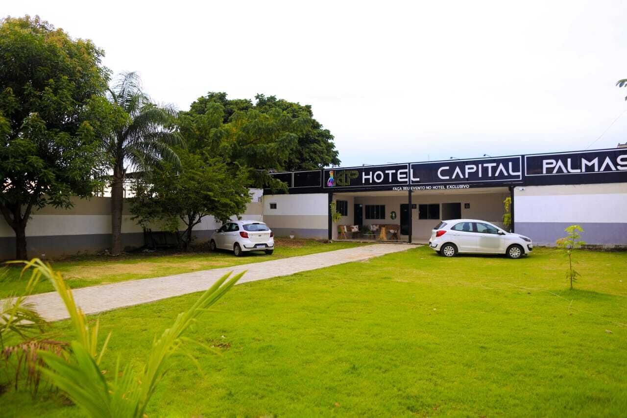 Hotel llamado "Hotel Capital Palmas" con fachada moderna, entrada pavimentada y dos coches blancos estacionados adelante.