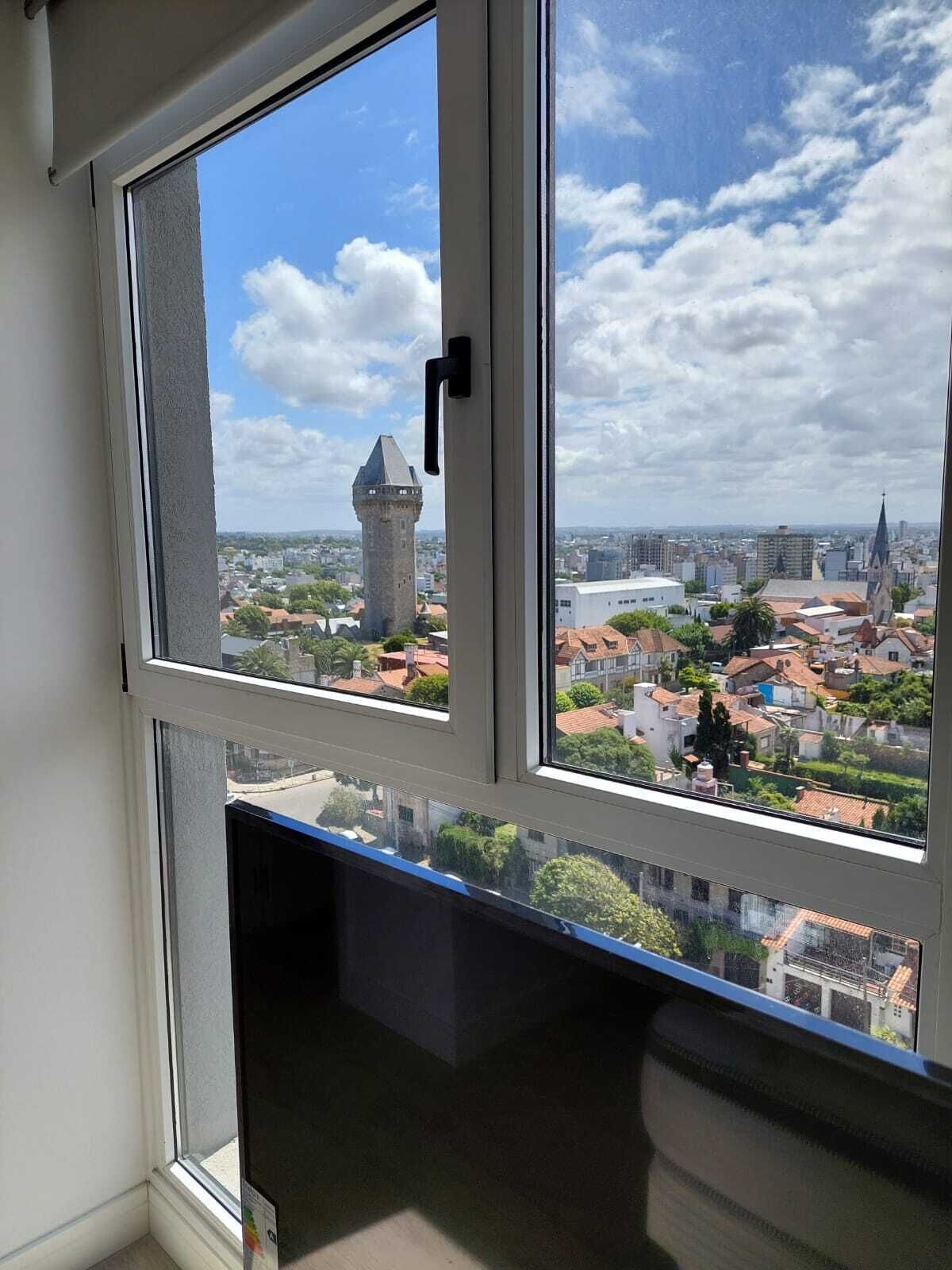 A room with a large window overlooking a cityscape, including a tower and various buildings.