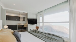A modern hotel room with a large bed, a TV, a desk, and a view of the city. - Residencias Roque Suarez (Mar del Plata)